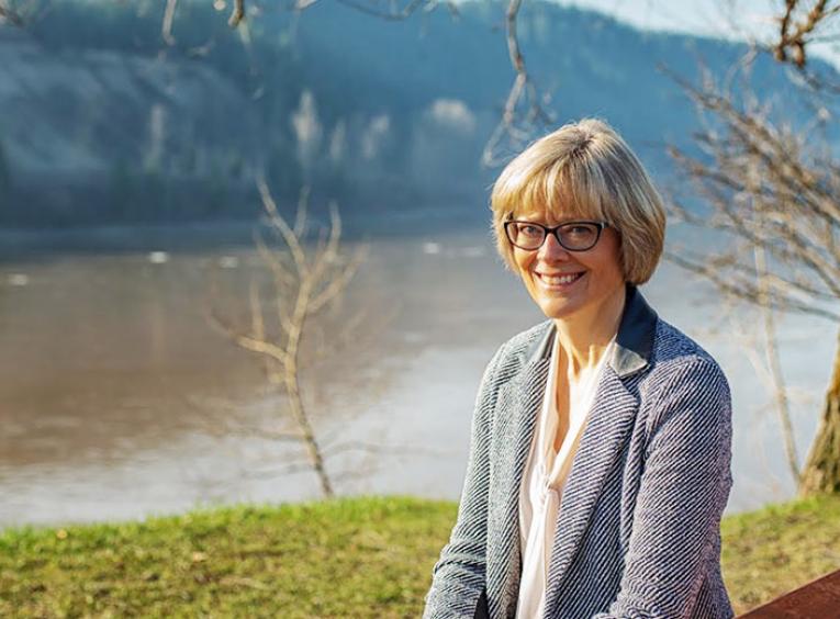 A woman smiles into the camera, a river behind her.