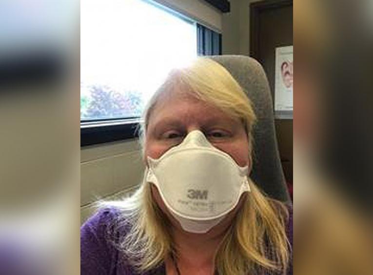 A woman looks into the camera, wearing an N95 mask.