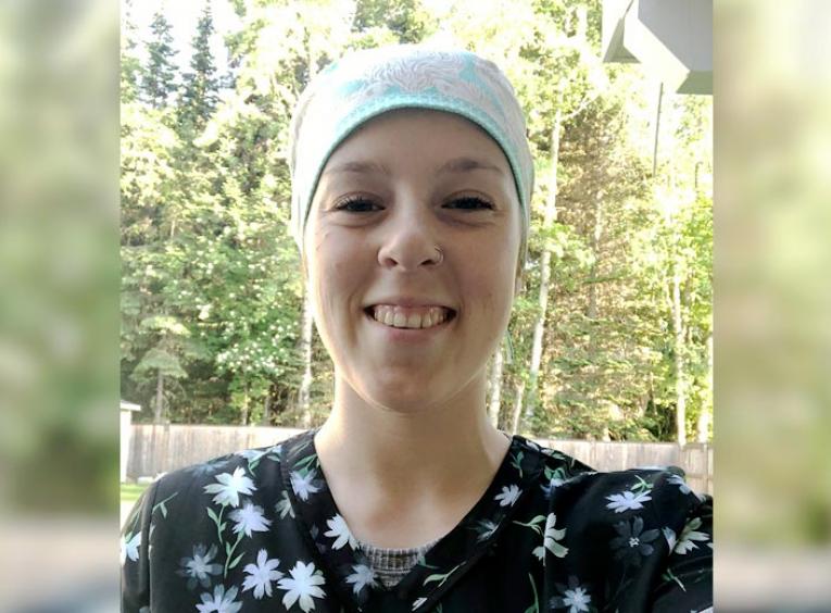 A young woman wearing medical scrubs and cap smiles into the camera.