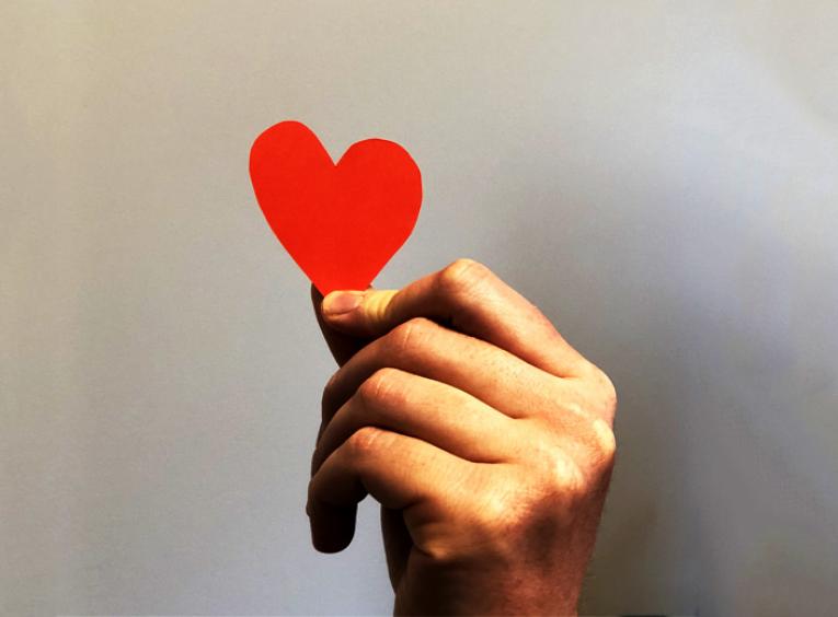 A hand holds a red construction paper heart.  