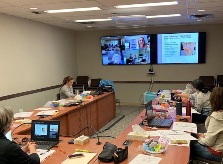 Four people sit in a meeting room, meeting with people over video chat.