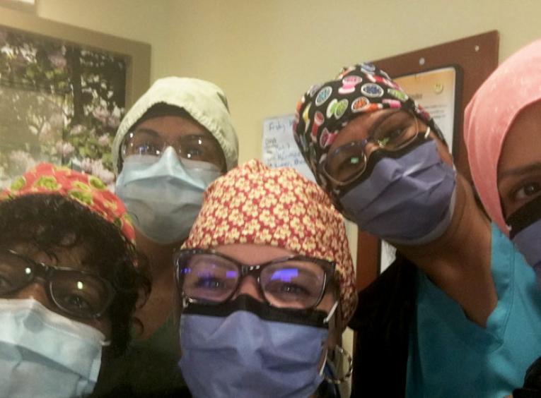 Five health care workers wearing masks and caps look into the camera.