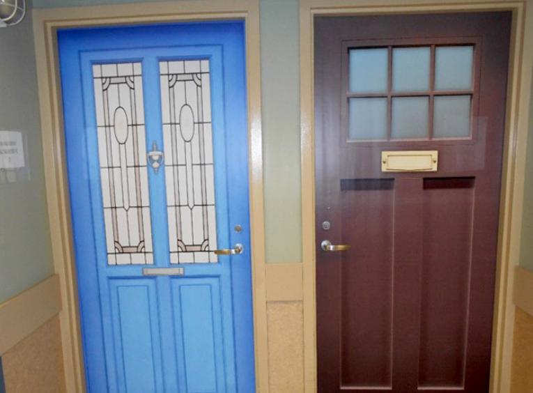 Two doors with different fake veneers. One is bright blue with long vertical windows. The other is brown with six small square windows near the top. 