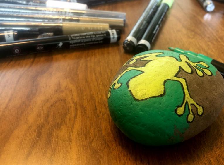 A rock has a yellow frog painted on it.