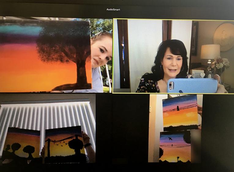 On a video chat, three youth hold up paintings while another person takes a picture.