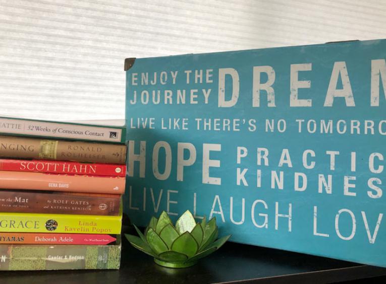 A stack of books is next to a sign with affirmations on it. 