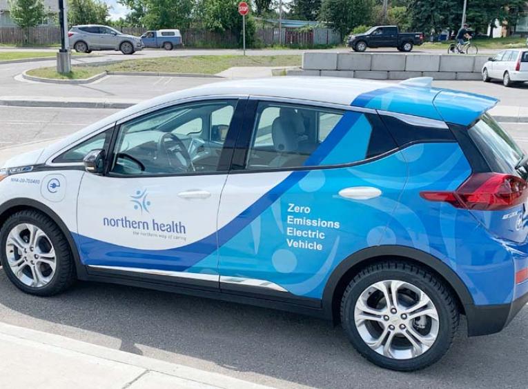 A Chevrolet Bolt with Northern Health decals is parked at a charging station.