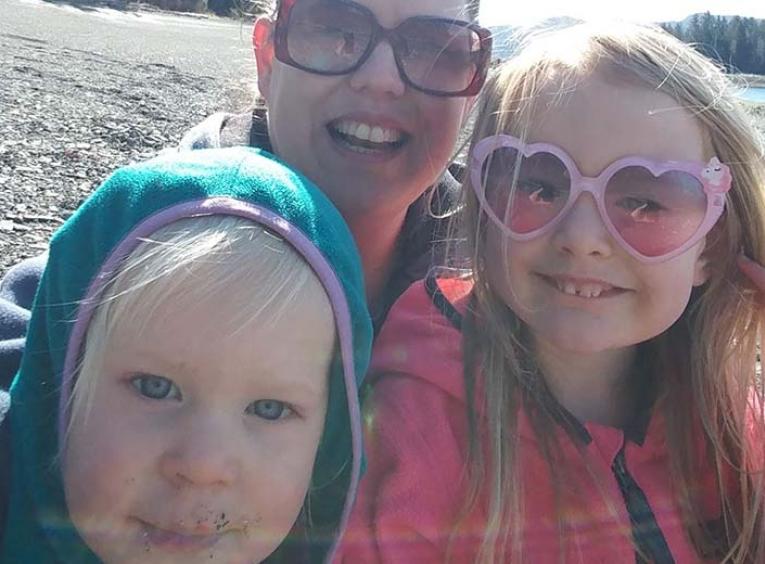 A woman in sunglasses and two children taking a selfie on a beach.