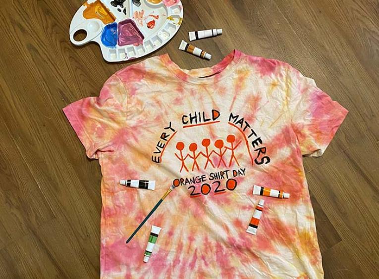 A tie-dye orange t-shirt decorated with paints for Orange Shirt Day 2020.