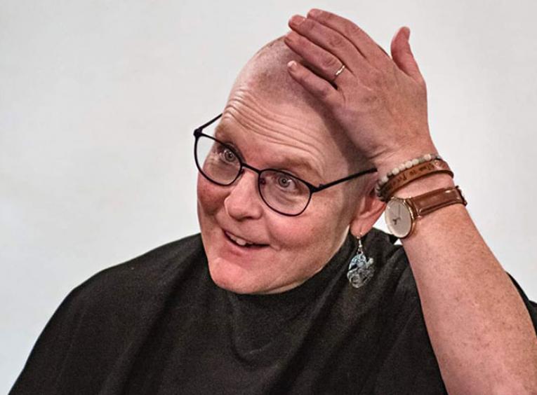 Woman with glasses touches head after having it shaved