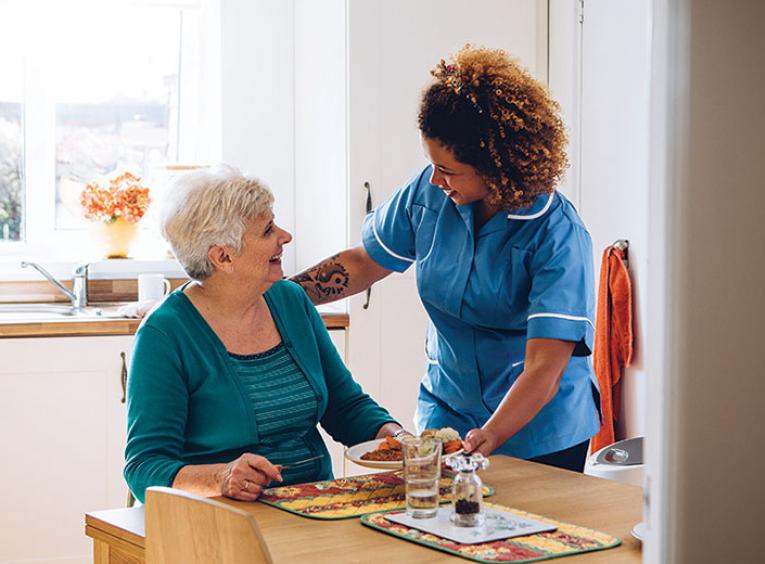 Home support worker stands at dinner table next to elderly woman