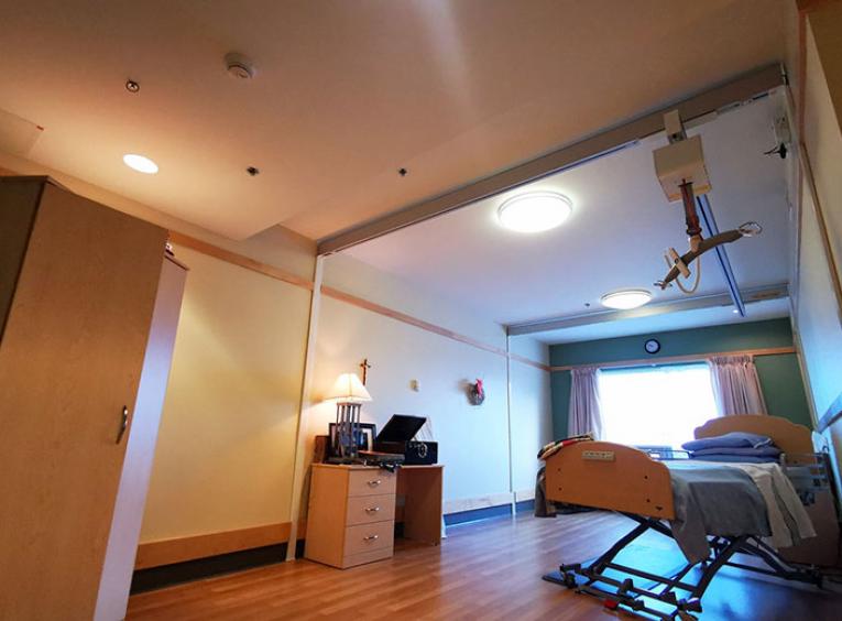 A bed in a long term care facility with a mechanical lift over it. 