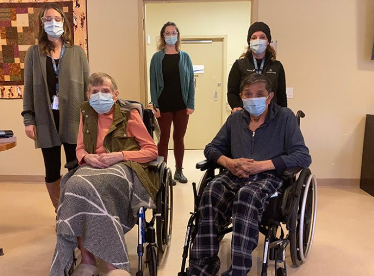 Three nurse immunizers stand behind two long-term care residents in wheelchairs.