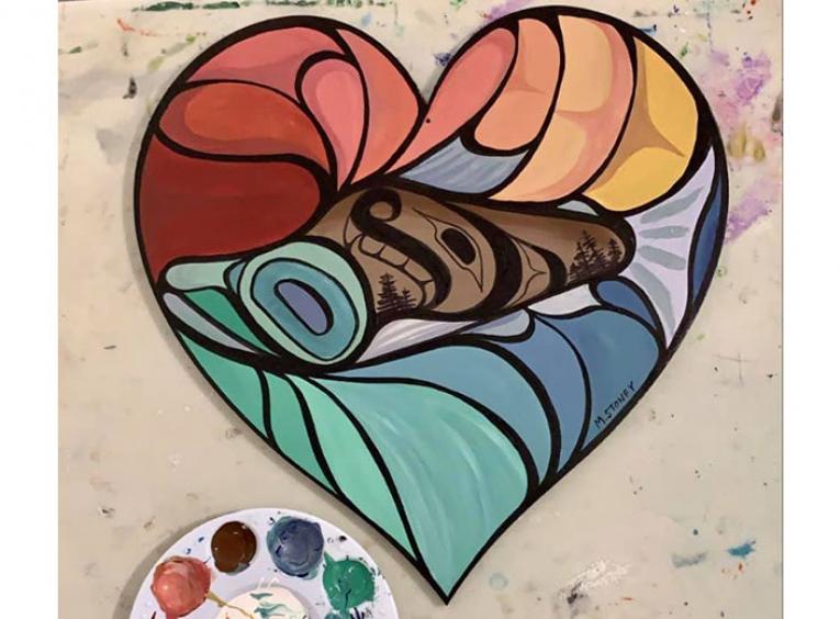A colourfully painted wooden heart with Indigenous images on it.