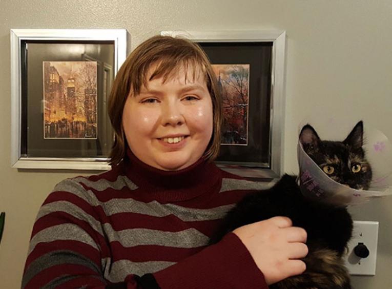 Woman smiles at camera while holding a black cat