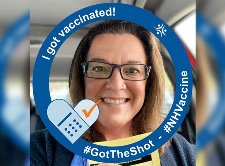 Woman smiling holding her vaccination card with Northern Health COVID-19 vaccination graphic.