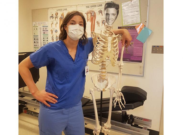 Woman in scrubs stands next to skeleton.