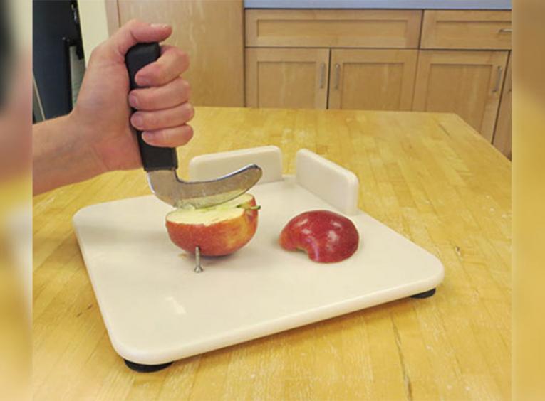 Person cutting an apple on a white cutting board with one hand.