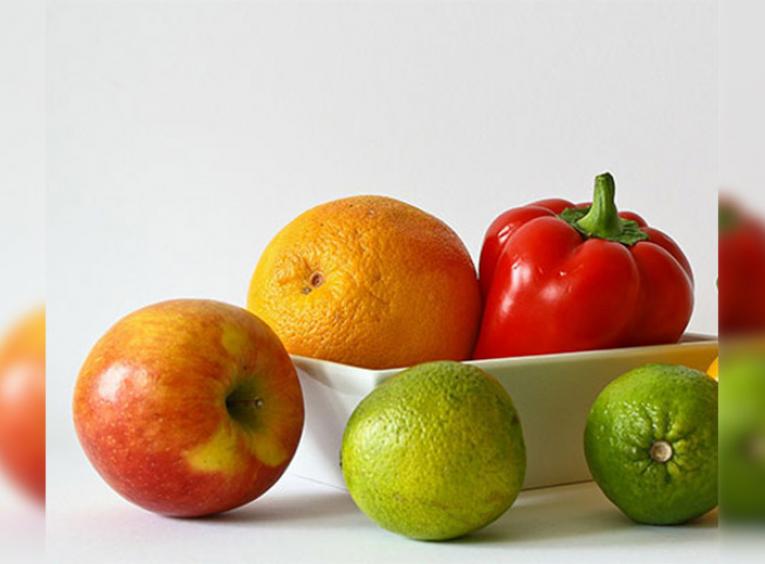 Apple, orange, lime, and red pepper in a white bowl