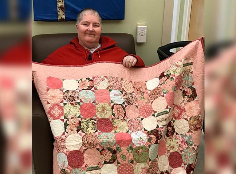 Smiling woman holding up a pink quilt.