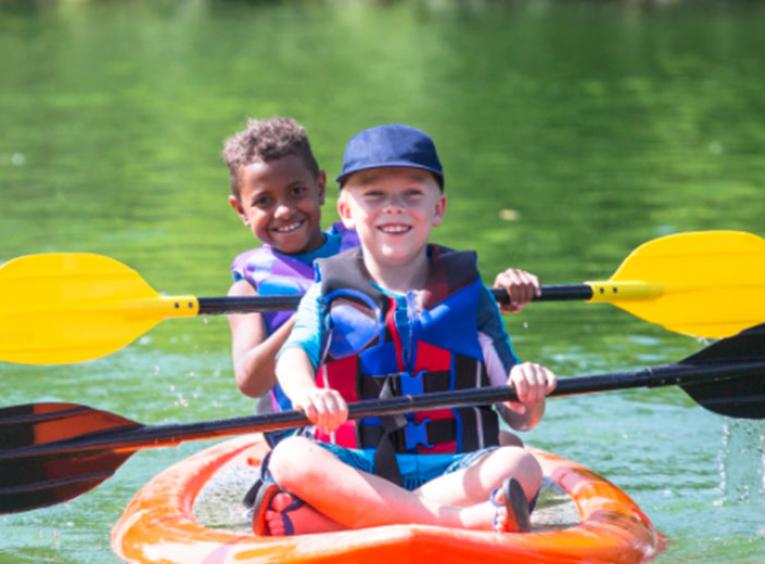 Two young children paddle in a kayak on the water.