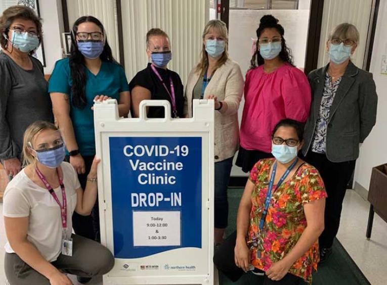 Group of women wearing masks stand next to a COVID-19 clinic sign