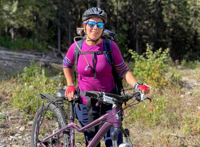 Woman in purple shirt standing beside her bicycle.