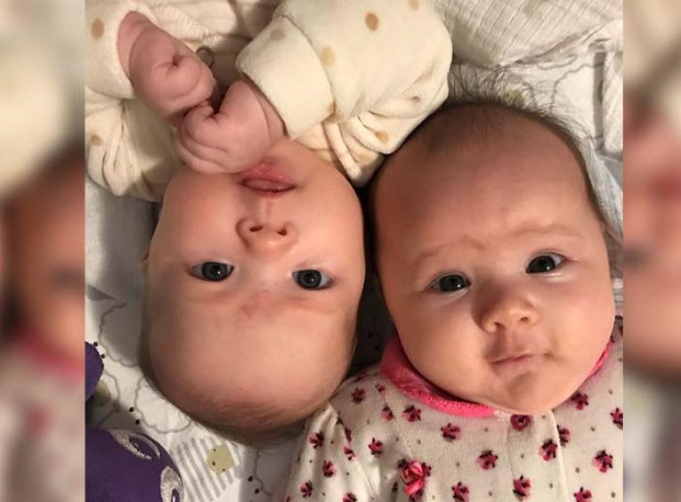 two twin baby girls look into the camera while laying down