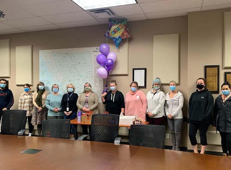 A group of people stand in a line wearing masks to celebrate the one year anniversary of the virtual clinic