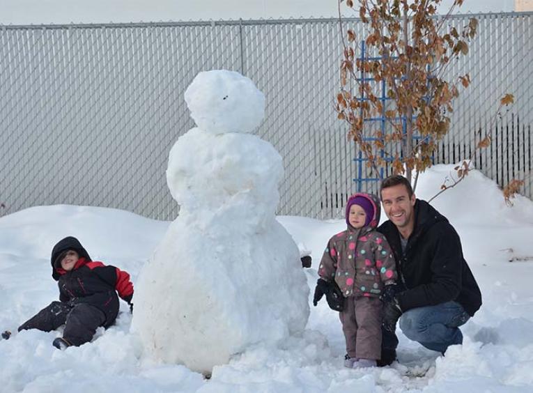 a man and two children pose in front of a snowman