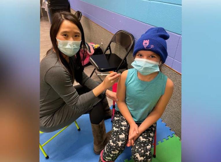 Masked health care worker gives a vaccine to a masked child