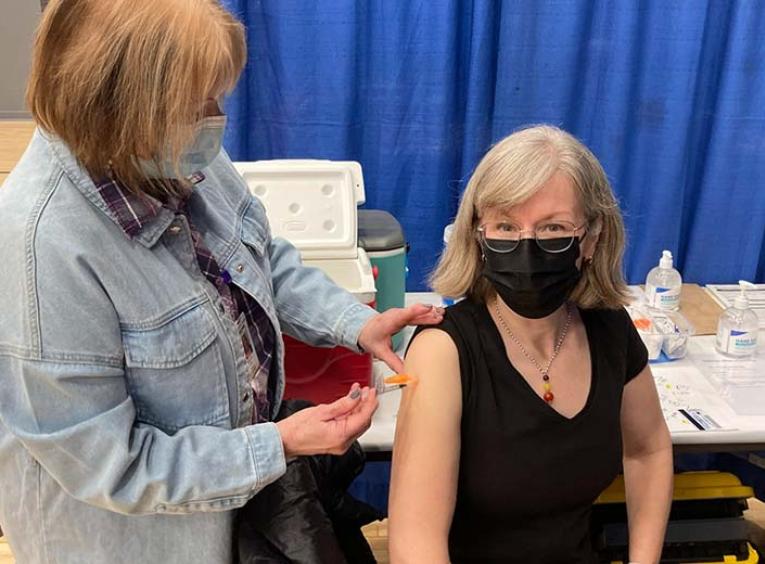 a nurse is shown administering a vaccine to the arm of a woman with shoulder length grey hair