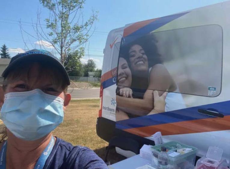 Woman wearing a mask stands in front of a health care van