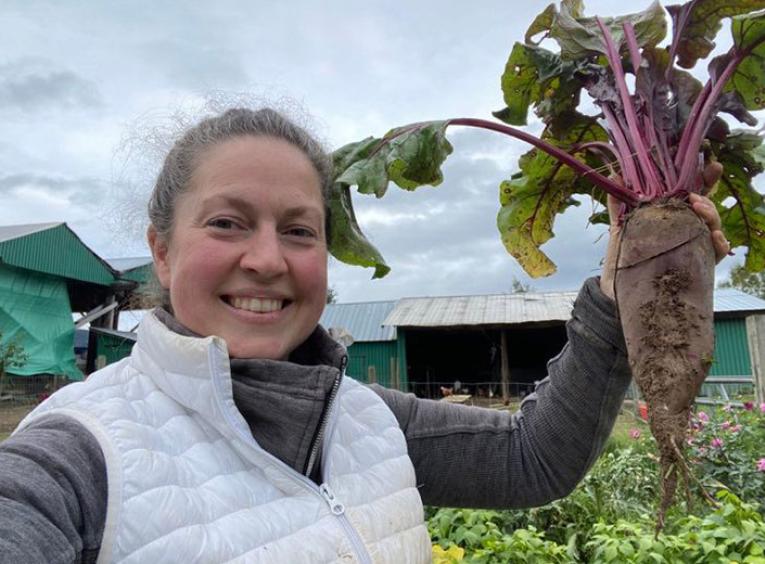 woman holds up large beet and smiles
