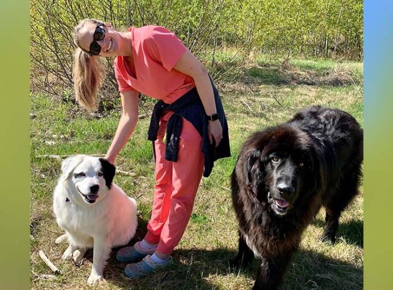 a woman with blonde hair is outside wearing pink scrubs standing next to one white dog and one black dog 