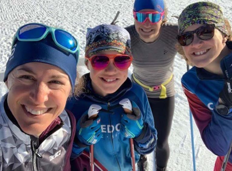 four women stand outside in the snow wearing skiing gear 