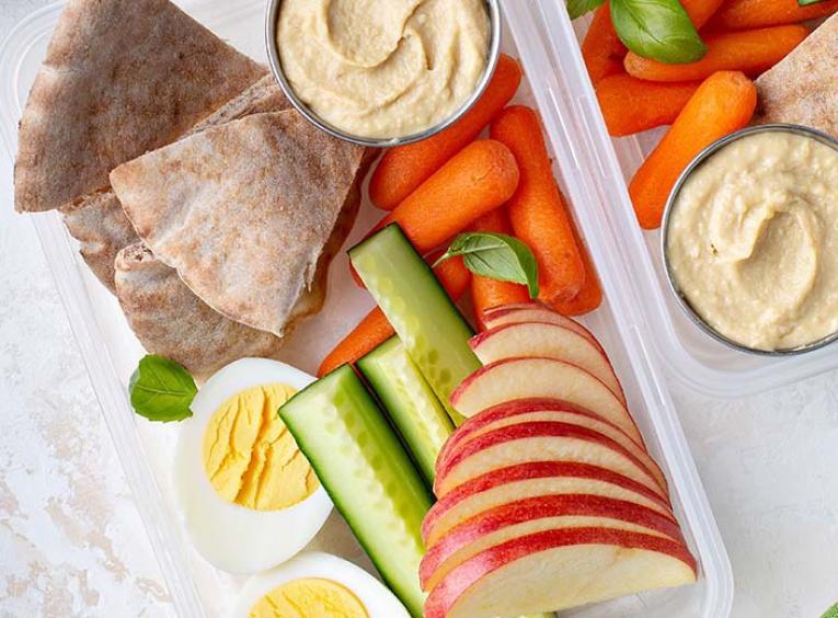 lunch container with sliced apple, hummus, pita bread, veggies and a boiled egg