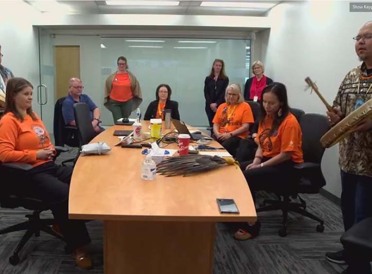 a group of people wearing orange shirts sit around a board room table