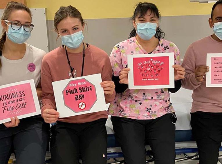 Nurses sit on a gurney holding anti-bullying, Pink Shirt Day signs 