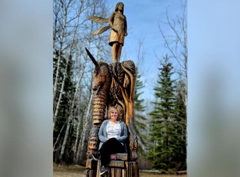 Darlene Danco sits on a chainsaw wood carving in Chetwynd BC. 