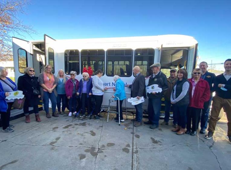 Group of people stand in front of a bus and cut a ribbon