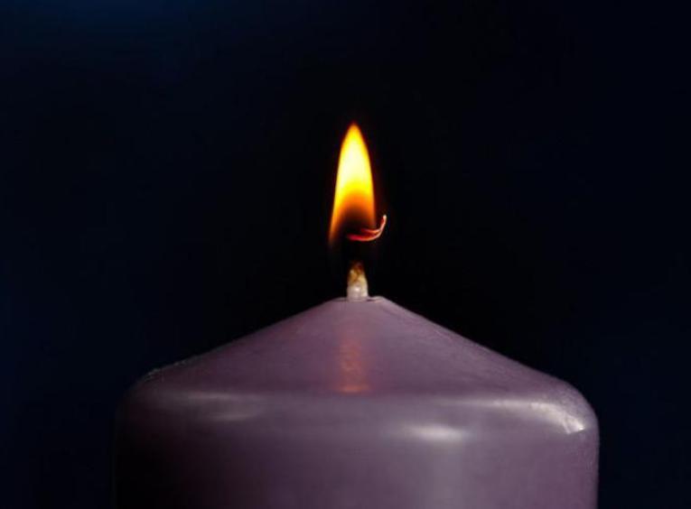 Purple candle with flame in front of a dark background.