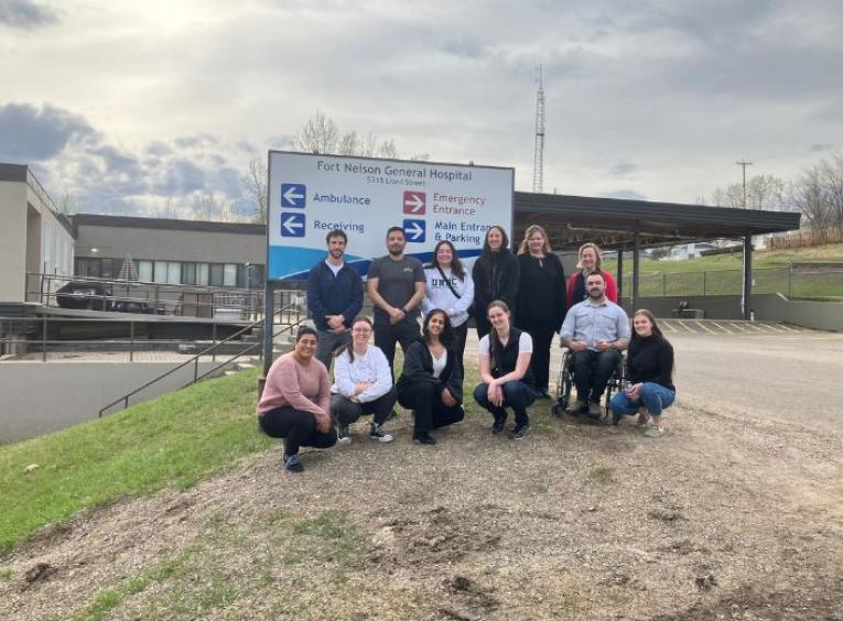 Students pose beside the entrance sign at the Fort Nelson Hospital