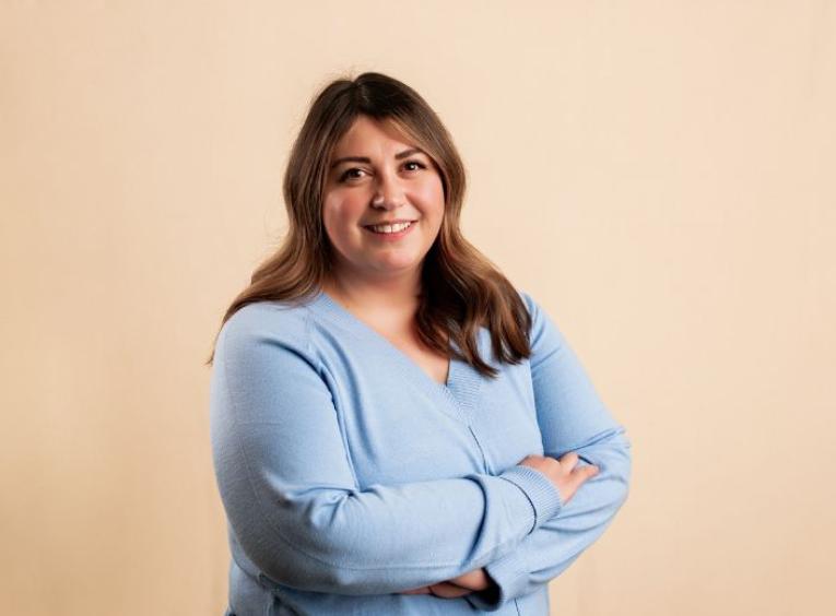 Lyndsey Rhea posing in a blue shirt against an orange background