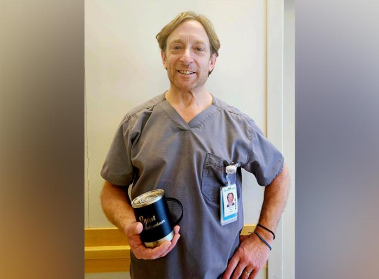 Male nurse stand in hallway holding an engraved cup