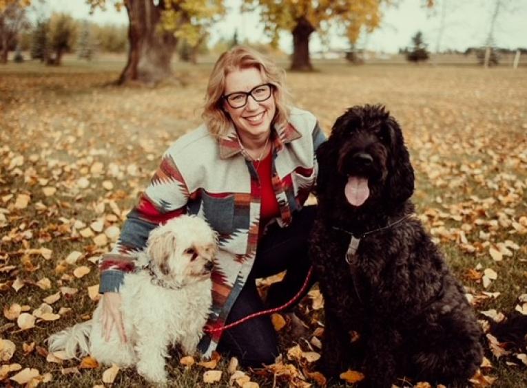 Woman poses with her dogs and the ground is covered in leaves.