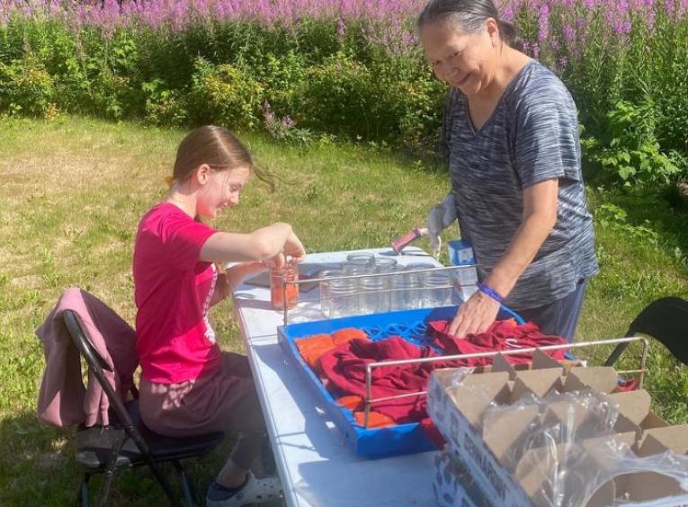 Two women at a picnic table as they dry and can salmon filets