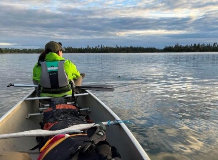 Maggie Kotowich sits at the front seat of a canoe over calm waters