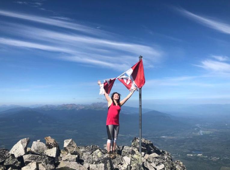 Savana standing atop a mountain holding onto a torn Canadian flag above her head