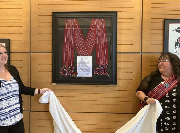 Kristen Scrivens and Bernadette Chaboyer standing beside a red, framed sash hung on the wall.